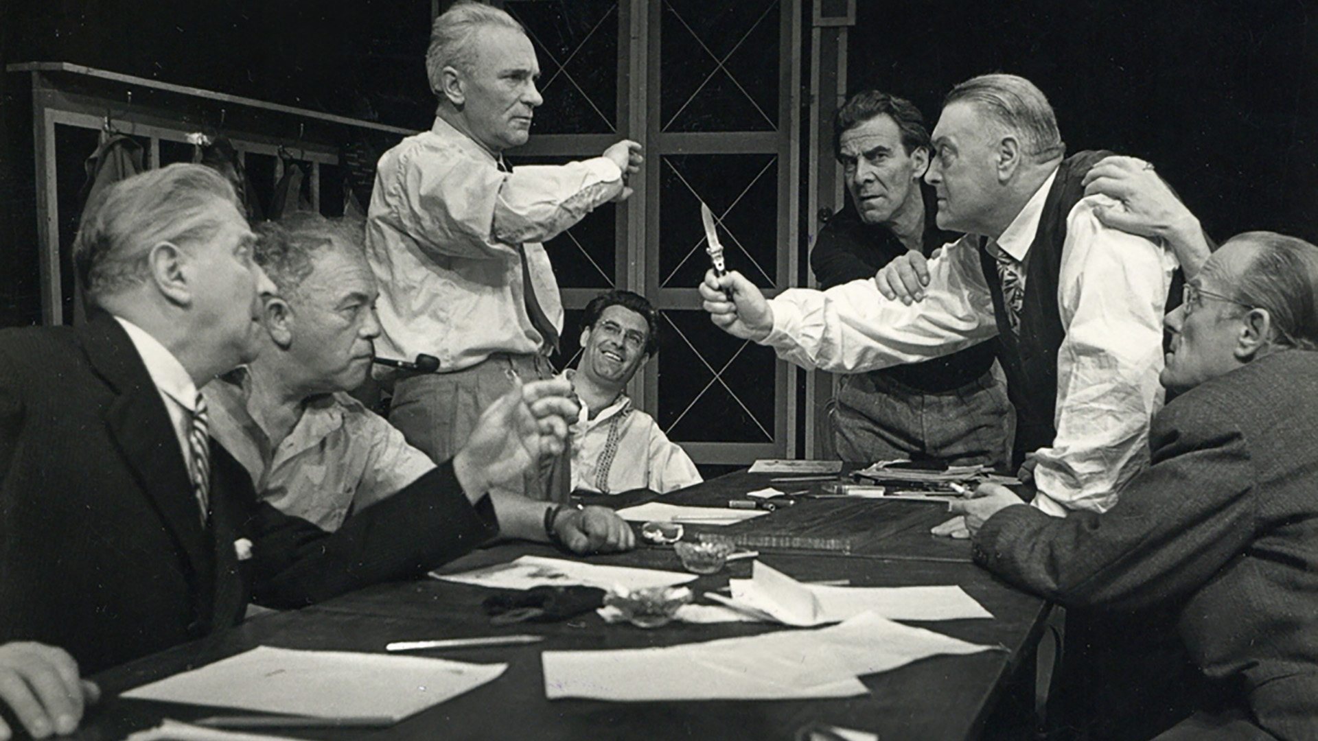 Stage photo from a 1959 Ljubljana Drama Theatre production of "Twelve Angry Men," showing diverse actors in intense discussion, representing unity through difference.